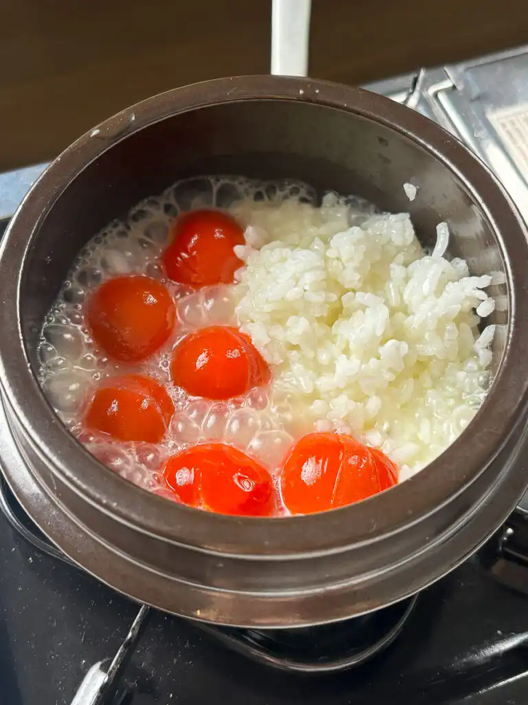 Tomato Rice Recipe: 10 Min Easy Cheesy Korean Pot Rice Spoon mashing softened cherry tomatoes against the inside wall of a cooking pot.