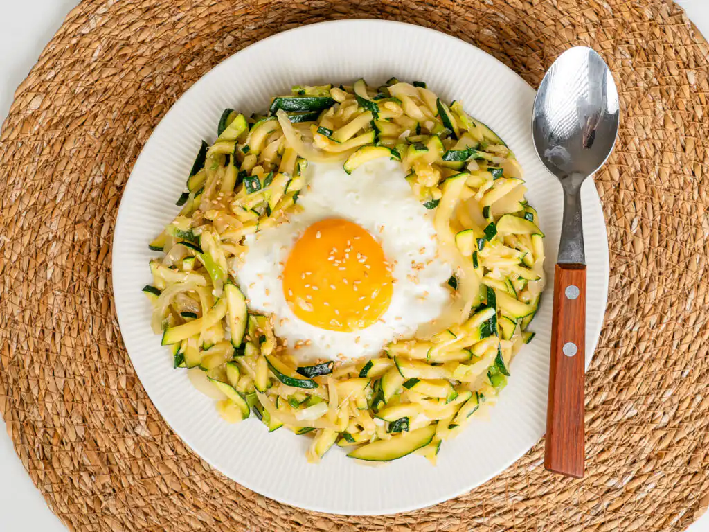 Korean Zucchini Rice Bowl: Easy Aehobak Deopbap Recipe orean zucchini rice bowl topped with a fried egg and sesame seeds in a ceramic bowl.