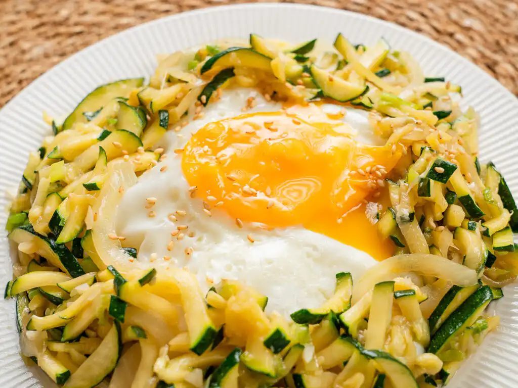 Korean Zucchini Rice Bowl: Easy Aehobak Deopbap Recipe Stir-fried zucchini and egg yolk being mixed together over warm steamed rice.
