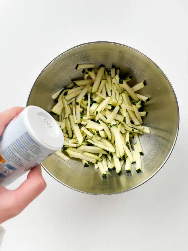 Korean Zucchini Rice Bowl: Easy Aehobak Deopbap Recipe ulienned zucchini sprinkled with sea salt in a glass mixing bowl.
