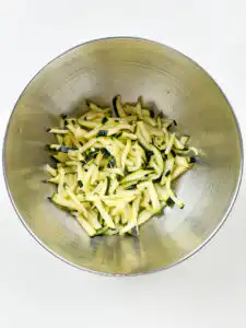 Korean Zucchini Rice Bowl: Easy Aehobak Deopbap Recipe Squeezing liquid out of salted zucchini slices by hand over a sink.