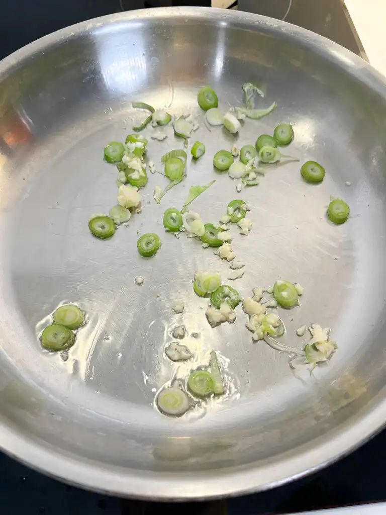 Sautéing minced garlic and green onions in olive oil in a frying pan over low heat.