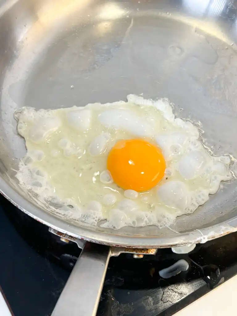 Frying a sunny-side-up egg in a hot pan with olive oil.