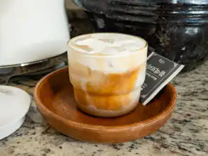 Viral Korean Barley Tea Latte: Easy Boricha Latte in 5 min A glass of iced barley tea latte placed on a marble kitchen countertop.