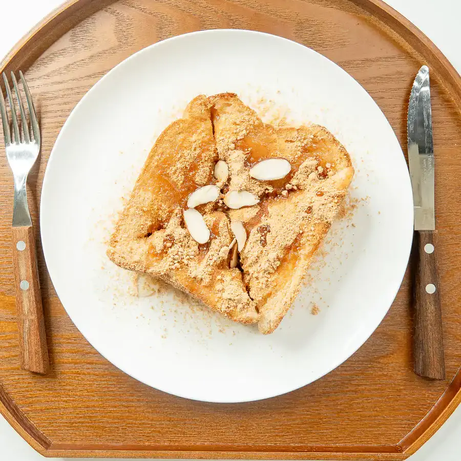 5 Min Injeolmi Toast: Easy Sulbing Toast with Korean Rice cake Golden injeolmi toast cut into four quarters topped with roasted soybean powder, sliced almonds, and honey drizzle