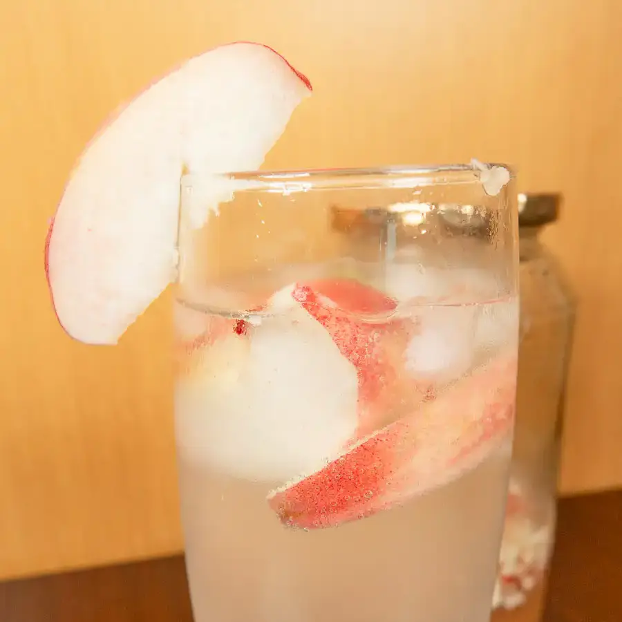 Korean Peach Syrup (Peach Cheong Recipe) for Peach Ade Korean peach syrup in a sterilized glass jar next to a tall glass of iced peach ade on a wooden table.