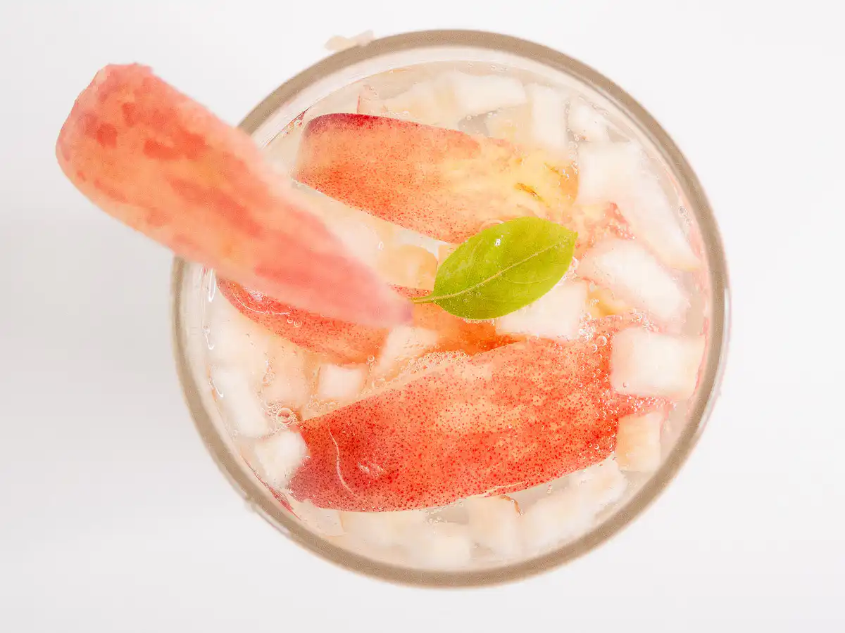 Korean Peach Syrup (Peach Cheong Recipe) for Peach Ade Korean peach ade garnished with a fresh peach slice on the glass rim and mint leaves on top.