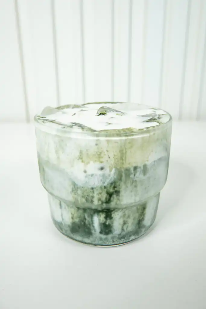 Vertical close-up of a Korean Mugwort Latte, with cream foam and mugwort gradient filling the frame