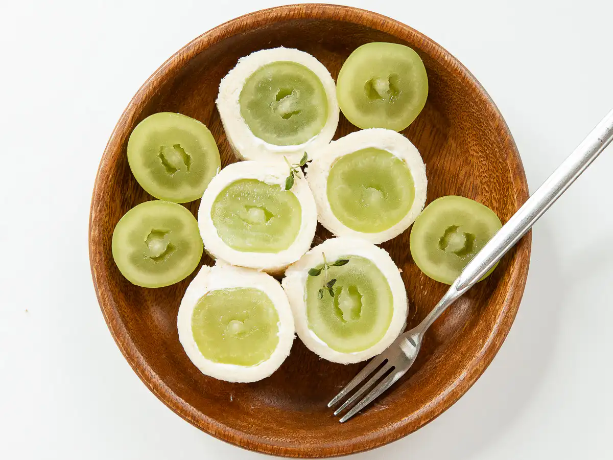 Close-up shot of crisp grapes inside a fruit roll sandwich served with a dessert fork on white marble.