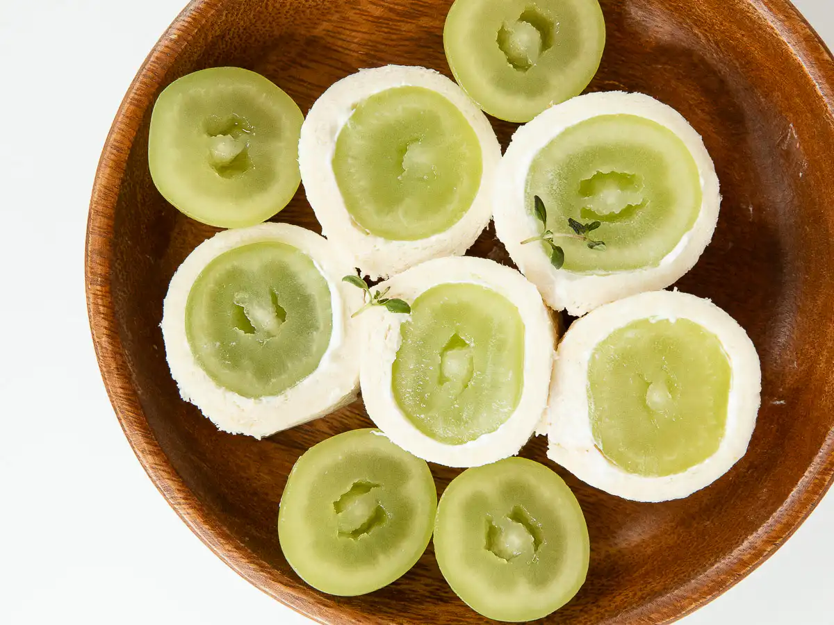 Shine Muscat Roll Sandwich: Easy Korean Shine Muscat Dessert A wooden dish holding a halved fruit roll sandwich topped with a sprig of fresh thyme.