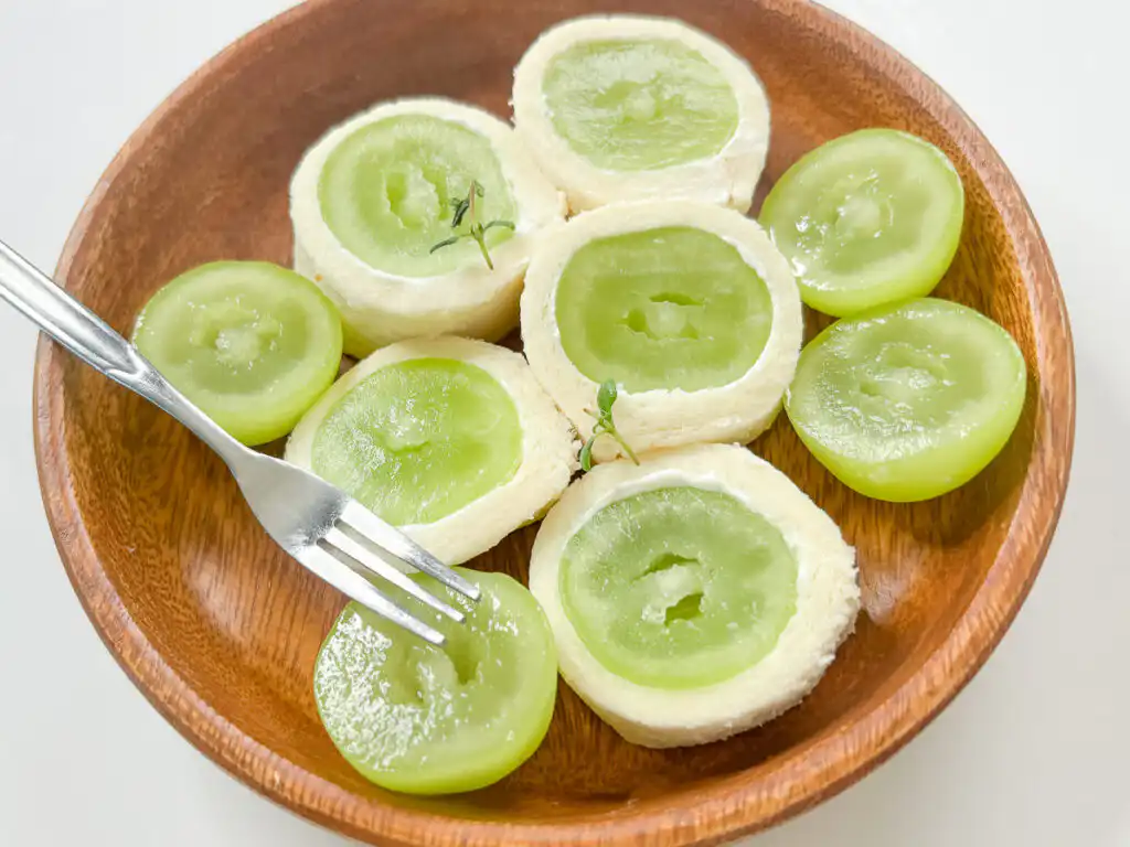 Shine Muscat Roll Sandwich: Easy Korean Shine Muscat Dessert Close-up of a dessert fork pressing near a soft fruit roll sandwich on a marble platter.